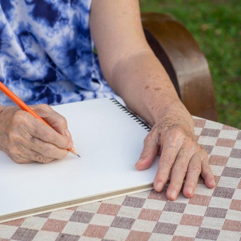 Hands of a senior woman writing a book while sitting on a chair