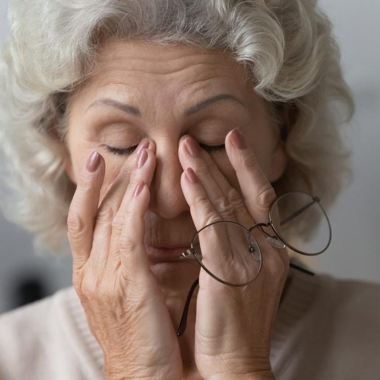 Tired mature woman rubbing nose bridge after taking off eyewear.
