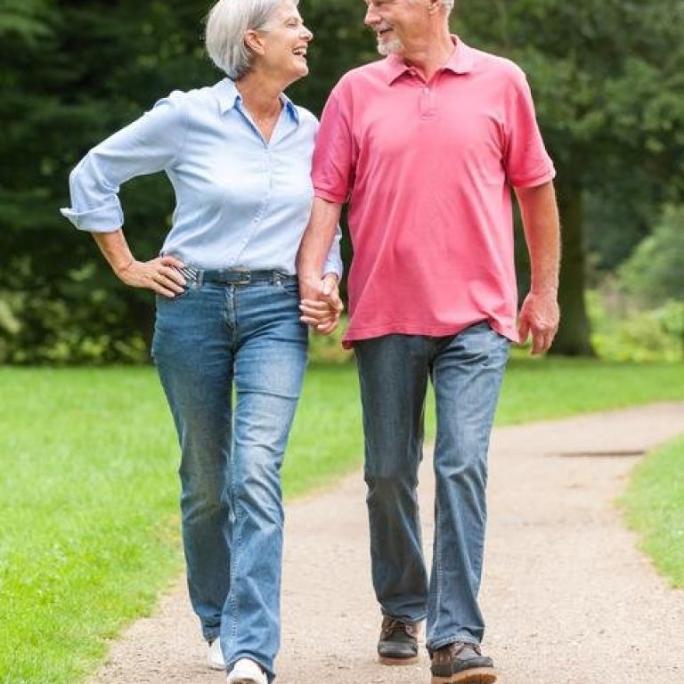 A senior couple holding hands walking in the park