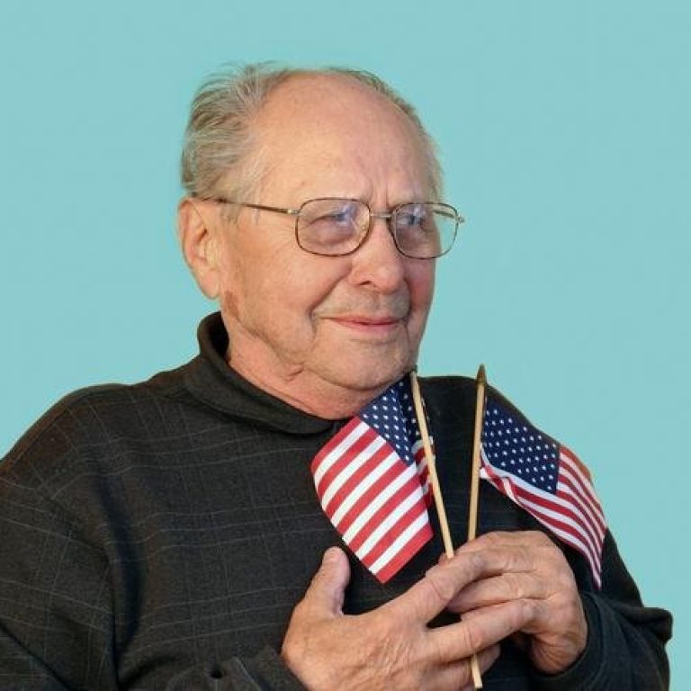 Old white man with two American flags on teal background